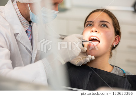 Male doctor dentist in white coat uniform treats girl patients teeth in dentistry. 133633396