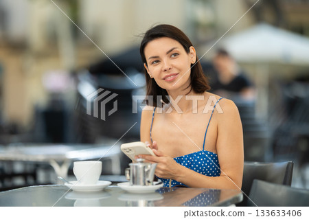 Young woman with phone drinking tea in cafe 133633406