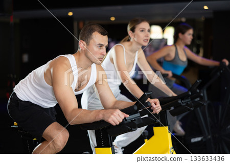 Man performs exercises with stationary bicycle in gym Man performs exercises with stationary bicycle in gym 133633436