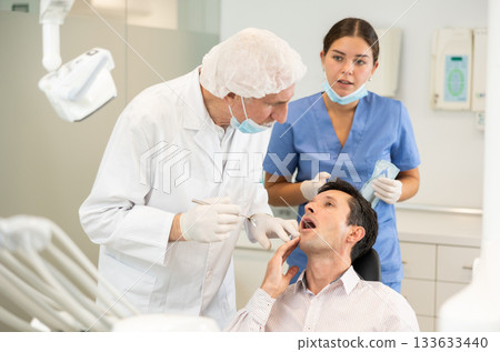 Elderly male dentist with nurse examining male patient Elderly male dentist with nurse examining male patient 133633440
