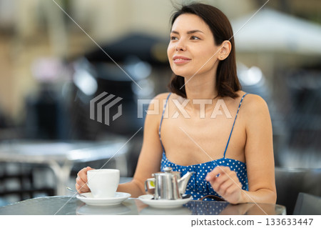 Stylish young brunette woman drinking tea while sitting on terrace of street cafe Stylish young brunette woman drinking tea while sitting on terrace of street cafe 133633447