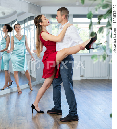 Couple in stage costumes learns tango dancing during individual lesson 133633452
