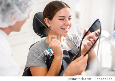 Man specialist holds mirror in front of girl patient and suggests evaluating effect of treatment Man specialist holds mirror in front of girl patient and suggests evaluating effect of treatment 133633456