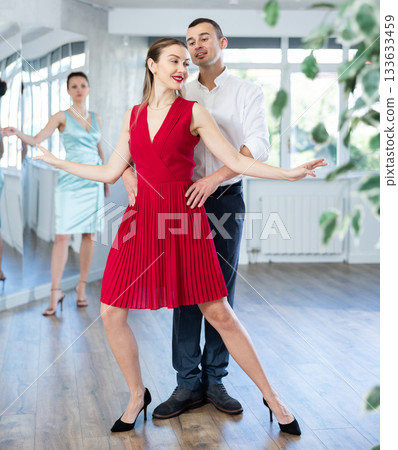 Man practicing samba with female partner in red in dance class 133633459