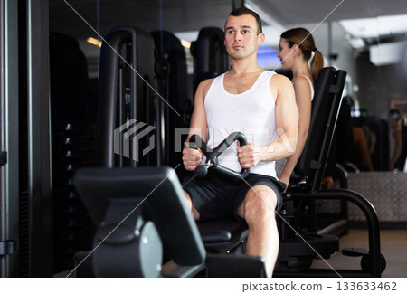 Sportive young guy training his arms using cable exercise machine in gym Sportive young guy training his arms using cable exercise machine in gym 133633462