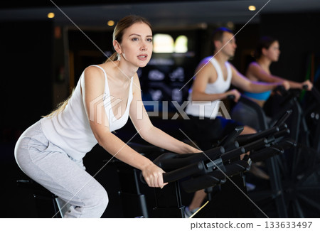 Sportive young girl doing spin bike exercises in well-equipped gym Sportive young girl doing spin bike exercises in well-equipped gym 133633497