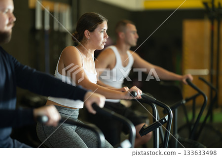 Sportive young girl doing air bike exercises in well-equipped gym Sportive young girl doing air bike exercises in well-equipped gym 133633498