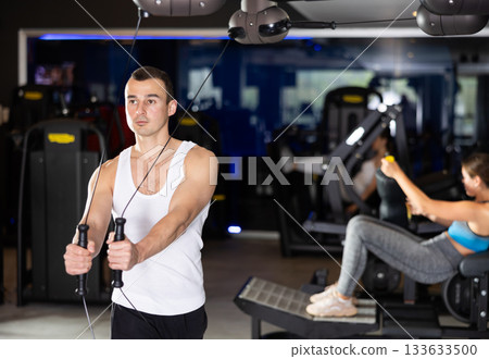 Active athlete young man during exercises on crossover exercise machine with loops and weighting 133633500