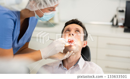 Young female dentist examining male patient 133633501