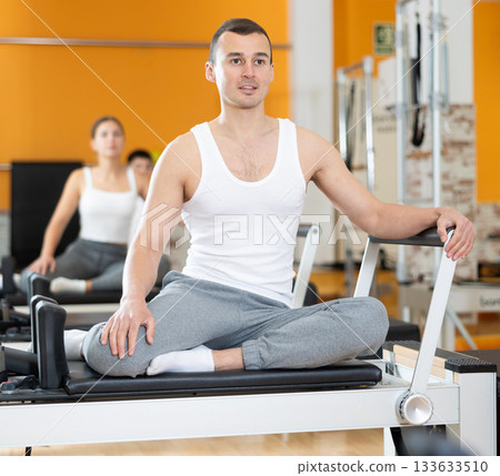 Man doing stretching exercises on Pilates reformer in fitness center 133633510