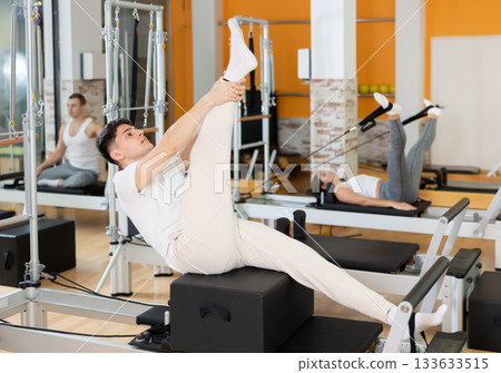 Guy doing stretching exercises on pilates reformer with sitting box 133633515