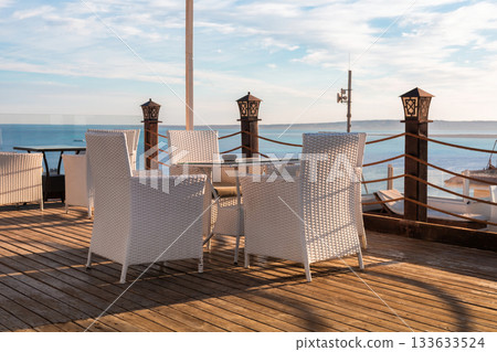 Seaside patio with white wicker chairs overlooking a tranquil ocean view 133633524