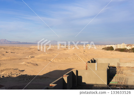 Expansive desert landscape with building shadows and mountainous horizon under blue sky 133633526
