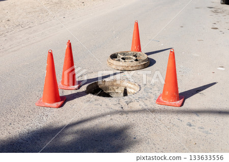 Caution on the road: safety cones surrounding open manhole for repair alert 133633556