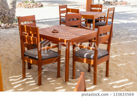 Cozy outdoor seating area in sunny beach environment with wooden table and chairs 133633569