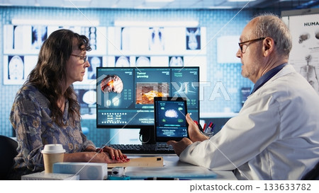 Meeting between doctor and patient to examine MRI scan showing a tumor, exploring treatment options, including immunotherapy, chemotherapy and preventative medicine. Risk factors. Camera A. Meeting between doctor and patient to examine MRI scan showing a tumor, exploring treatment options, including immunotherapy, chemotherapy and preventative medicine. Risk factors. Camera A. 133633782
