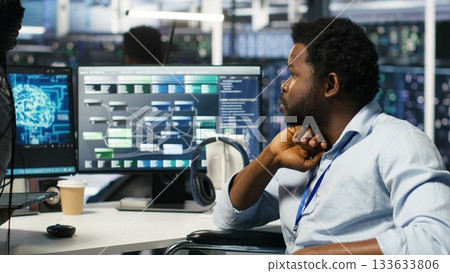 Data center engineer in wheelchair and colleague oversee automated tasks using node tree programming tool. Inclusive server farm team adjusts system settings based on AI analytics, camera B Data center engineer in wheelchair and colleague oversee automated tasks using node tree programming tool. Inclusive server farm team adjusts system settings based on AI analytics, camera B 133633806