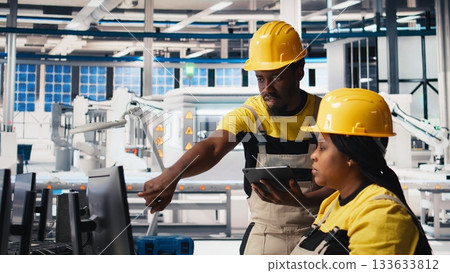 Black employees analyzing production line solar panels in the photovoltaics factory, analyzing data. Manufacturing plant engineers reading documentation files to troubleshoot errors. Camera B. 133633812