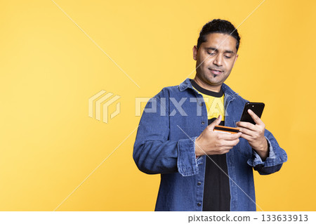 Indian male model excited about online shopping on website with his credit card, checking his balance and processing the payment for things on sale. Young adult entering banking credentials. 133633913