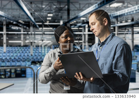 Data center computer scientists doing brainstorming, using laptop to manage system stability. Server room colleagues optimizing performance with device, configuring equipment 133633940