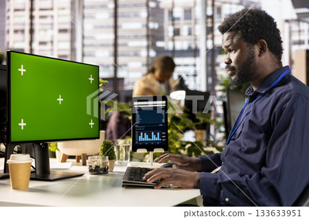African american office worker verifying data analytics with copy space, using monthly infographics to create a financial report. Young man collecting performance metrics on computer. 133633951