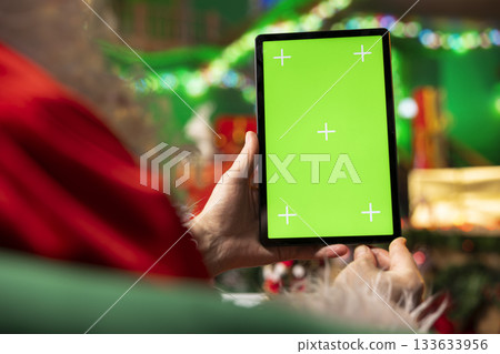 Man wearing Santa costume using mockup tablet in workshop to check messages from kids worldwide. Father Christmas enjoying winter holidays wishes sent by children via email using chroma key device Man wearing Santa costume using mockup tablet in workshop to check messages from kids worldwide. Father Christmas enjoying winter holidays wishes sent by children via email using chroma key device 133633956