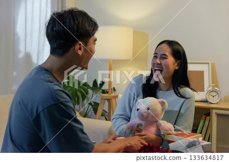 Happy young couple share love at home, man and woman enjoy romantic valentine day, exchanging thoughtful gifts, laughing together in special moment. Happy young couple share love at home, man and woman enjoy romantic valentine day, exchanging thoughtful gifts, laughing together in special moment. 133634817