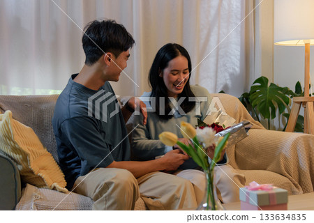 Happy young couple love at home, man gives woman romantic Valentine Day gift, roses for joyful anniversary celebration, showing deep affection and pure delight together. Happy young couple love at home, man gives woman romantic Valentine Day gift, roses for joyful anniversary celebration, showing deep affection and pure delight together. 133634835