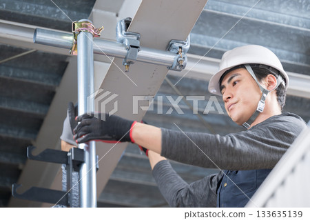 Construction work such as clamping single-pipe pipes on high scaffolding near the ceiling. Image of construction workers and workers Construction work such as clamping single-pipe pipes on high scaffolding near the ceiling. Image of construction workers and workers 133635139