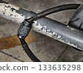 Close-up of a combination cable lock used to secure a motorcycle to a metal bar. Shows worn textures, numbers on the dial, and the sturdy cable, suitable for illustrating security, safety 133635298
