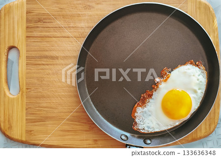 Stainless steel frying pan with a fried egg on a wooden table. Stainless steel frying pan with a fried egg on a wooden table. 133636348