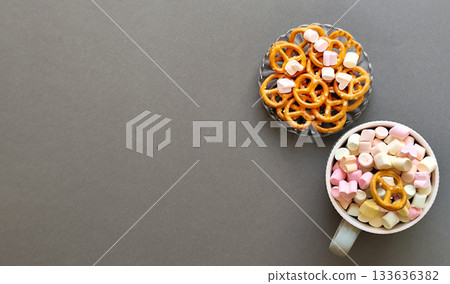 A bowl of marshmallows and pretzels on a gray background. Space for text, top view. A bowl of marshmallows and pretzels on a gray background. Space for text, top view. 133636382