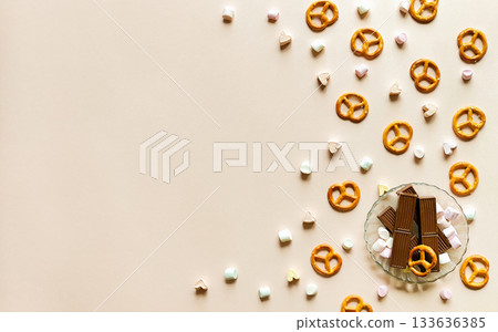 Marshmallows, chocolate, and pretzels on a beige background. Space for text, top view. Marshmallows, chocolate, and pretzels on a beige background. Space for text, top view. 133636385