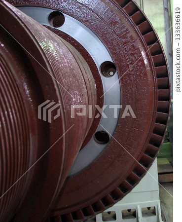 A detailed close-up of a large, red industrial turbine component, featuring grooved textures and circular openings. The image showcases the intricate design and powerful scale of heavy machinery 133636619