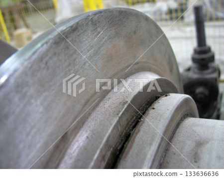 A closeup macro photography of a heavily worn metal part reveals scuffs, grooves, and traces of grease or oil. An industrial environment is blurred in the background. 133636636