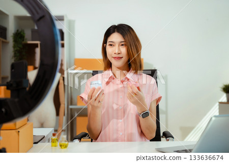 Asian vlogger woman influencer, SME retail store owner smile enjoy selling show live sale online screen smartphone and laptop work at home. 133636674