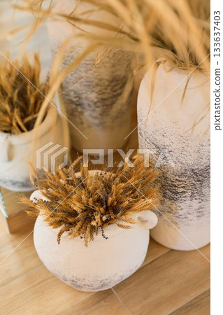 artisanmade ceramic vases filled with dried wheat displayed on wooden table in natural light 133637403