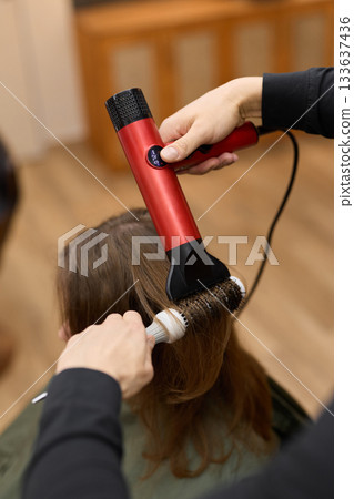 styling action captured, vibrant portrayal of stylist shaping hair amidst lively salon environment 133637436