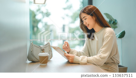 Adult asian business woman using digital tablet working and relax at cafe sitting near window Adult asian business woman using digital tablet working and relax at cafe sitting near window 133637511