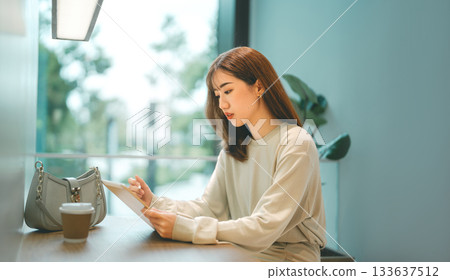 Adult asian business woman using digital tablet working and relax at cafe sitting near window 133637512