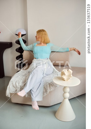 candid shot capturing blonde woman reaching toward artistic lamp beside textured skirt and sofa candid shot capturing blonde woman reaching toward artistic lamp beside textured skirt and sofa 133637519
