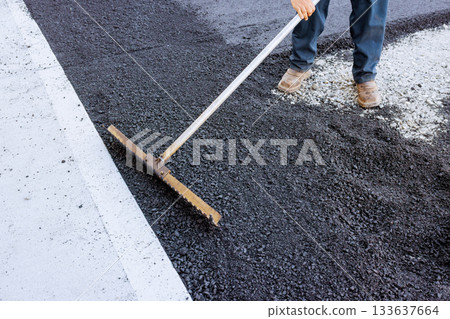 Worker levels freshly laid asphalt on road surface in construction site 133637664