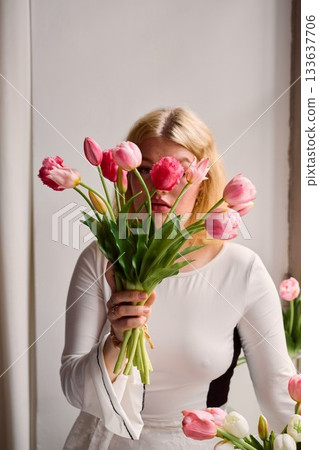 Female with light hair arranges pink and white tulips indoors Female with light hair arranges pink and white tulips indoors 133637706