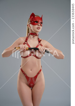 Woman poses confidently in leather belts in a studio setting with a sleek backdrop 133638445