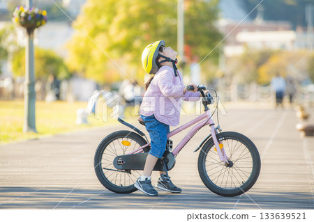 戶外景色：陽光明媚的公園裡，一個女孩騎著腳踏車抬頭望向天空。 133639521