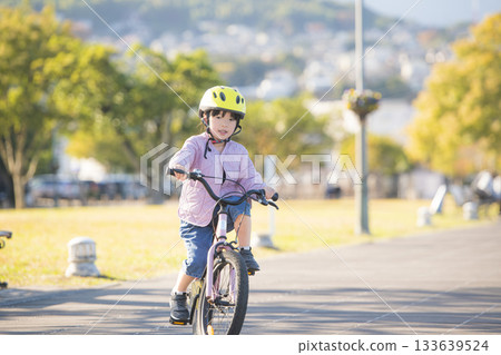 秋高氣爽的戶外景色，一位女孩騎著腳踏車沿著公園道路行駛。 133639524