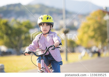 A lively outdoor activity where Japanese children wearing helmets practice riding bicycles 133639525