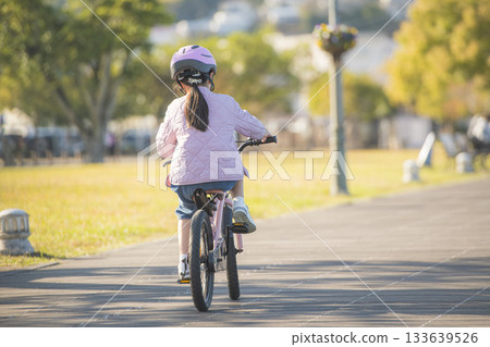 Rear view of a girl riding a bicycle on a park road Rear view of a girl riding a bicycle on a park road 133639526
