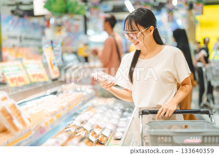 Young adult asian woman consumer choosing ready meals food japanese supermarket store choice buying 133640359