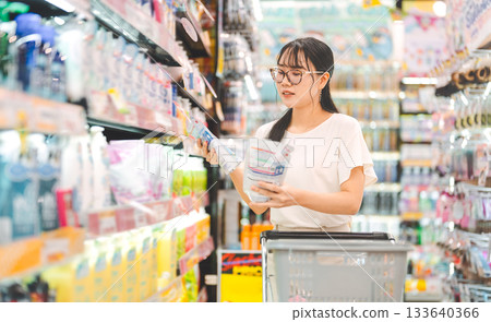 Young adult asian woman customer choosing laundry liquid detergent from household shelf shopping 133640366
